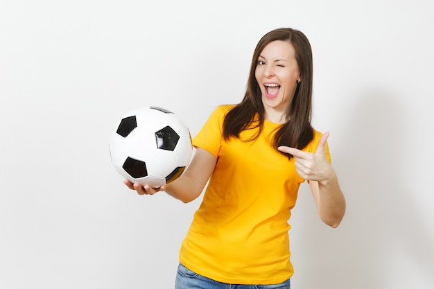 Beautiful european young cheerful happy woman, football fan or\
player in yellow uniform pointing on soccer ball isolated on white\
background. sport, play football, health, healthy lifestyle\
concept.