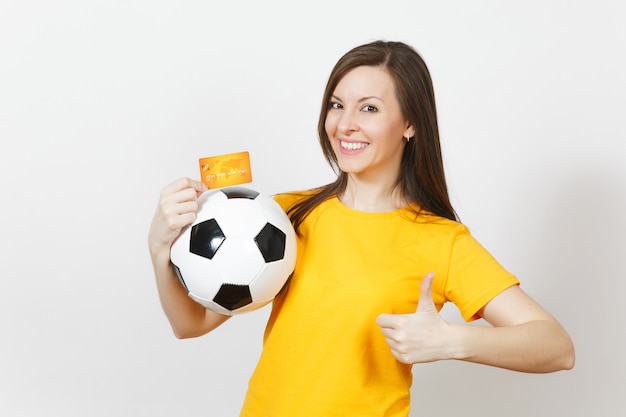 Beautiful european young cheerful woman, football fan or player\
in yellow uniform holding credit card soccer ball isolated on white\
background. sport, play football game, excitement lifestyle\
concept.