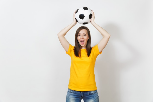 Beautiful european young cheerful woman, football fan or player\
in yellow uniform holding above head soccer ball isolated on white\
background. sport, play football, health, healthy lifestyle\
concept.