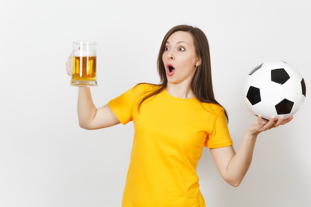 Beautiful european young cheerful woman, football fan or player\
in yellow uniform holding pint mug of beer, soccer ball isolated on\
white background. sport, play football, healthy lifestyle\
concept.