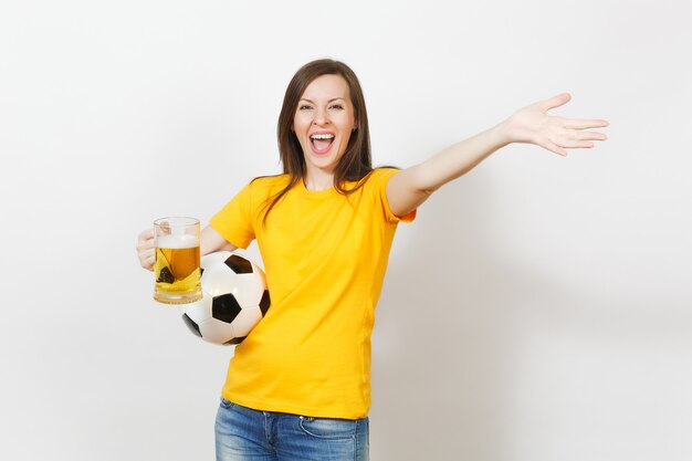 Beautiful european young cheerful woman, football fan or player\
in yellow uniform holding pint mug of beer, soccer ball isolated on\
white background. sport, play football, healthy lifestyle\
concept.