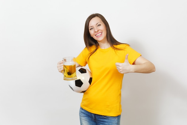 Beautiful european young cheerful woman, football fan or player\
in yellow uniform holding pint mug of beer, soccer ball isolated on\
white background. sport, play football, healthy lifestyle\
concept.