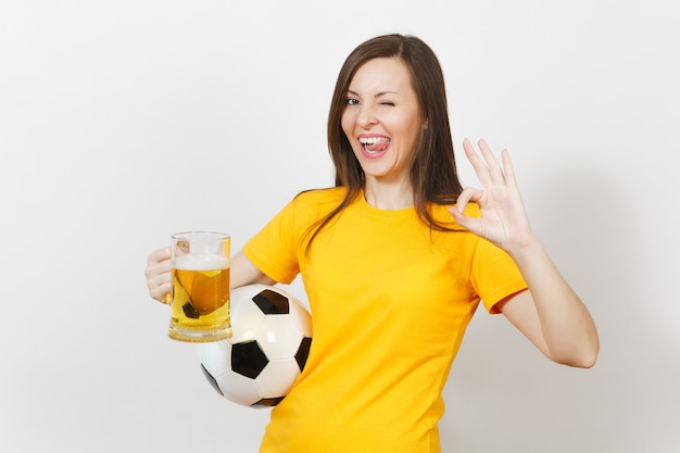 Beautiful european young cheerful woman, football fan or player\
in yellow uniform holding pint mug of beer, soccer ball isolated on\
white background. sport, play football, healthy lifestyle\
concept.