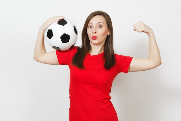 Beautiful European young strong slim woman, football fan or player in red uniform holding classic soccer ball isolated on white background. Sport, play football, health, healthy lifestyle concept.
