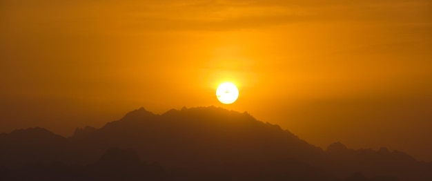 Beautiful evening panoramic landscape with bright setting sun over distant mountain peaks at sunset.