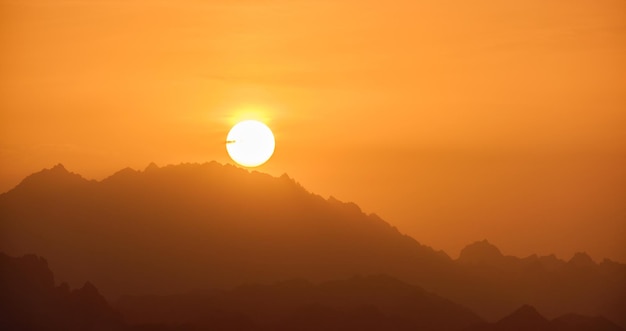 Beautiful evening panoramic landscape with bright setting sun over distant mountain peaks at sunset.