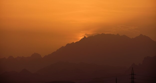 日没時に遠くの山の頂上に明るい夕日と美しい夜のパノラマの風景