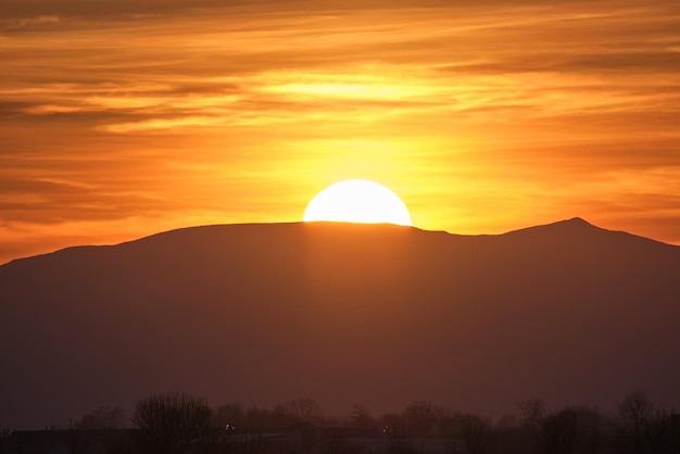 Beautiful evening panoramic landscape with bright setting sun over distant mountain peaks at sunset