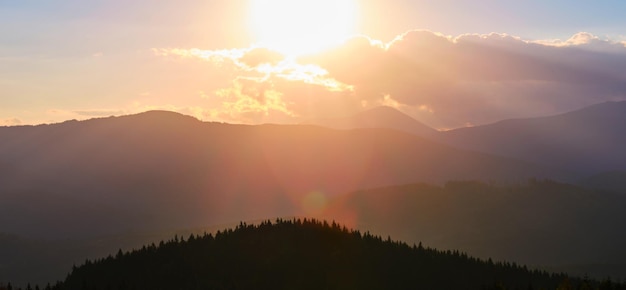 Beautiful evening panoramic landscape with bright setting sun over distant mountain peaks at sunset