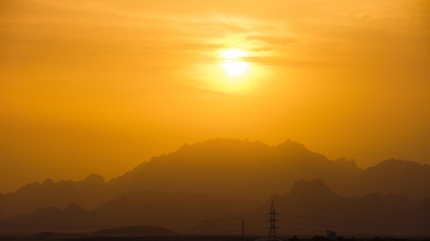 日没時に遠くの山の頂上に明るい夕日と美しい夜のパノラマの風景。