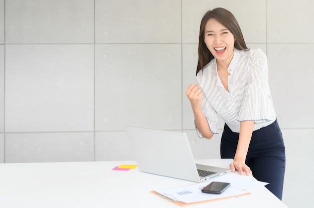 아름 다운 흥분된 아시아 여자 노트북 및 사무실에서 문서와 함께 성공 팔을 축 하합니다. 비즈니스 성공 개념