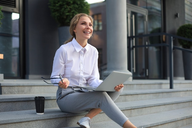 Beautiful excited business woman sitting near business center and using laptop.