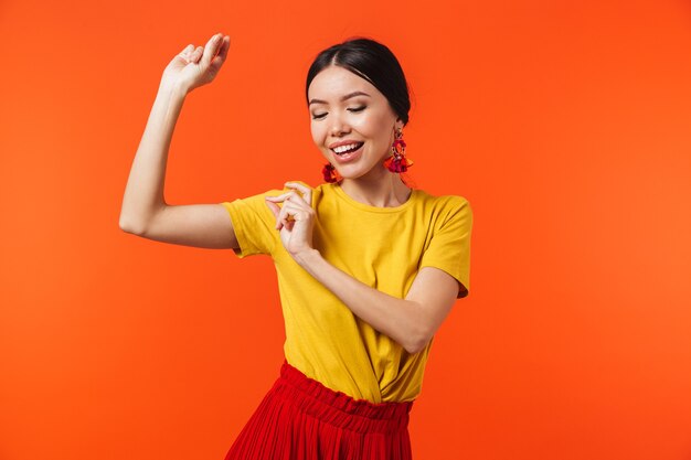 a beautiful excited happy young woman posing isolated over orange wall dancing.