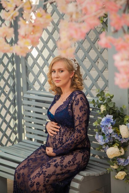 Beautiful expectant mother in a lace dress sits in a gazebo