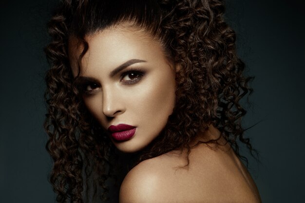 Beautiful face of a fashion model with black eyes.Curly hair. Red lips.