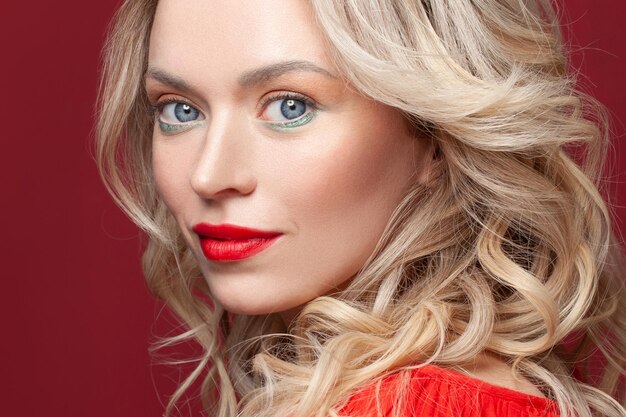 Photo beautiful face studio portrait nice woman with blonde curly hair and makeup on red background