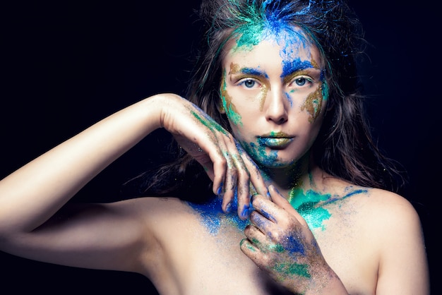 Photo beautiful face with colored paint on a black , beautiful girl, colorful makeup, fashionable woman, toned image,