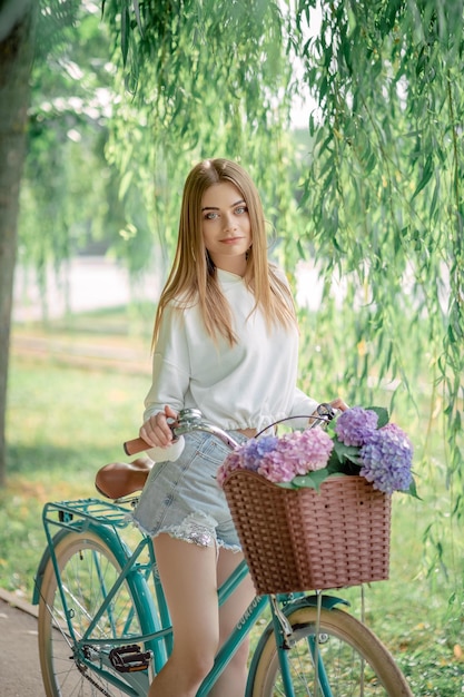 Bella ragazza dai capelli biondi su una bicicletta con fiori ortensie