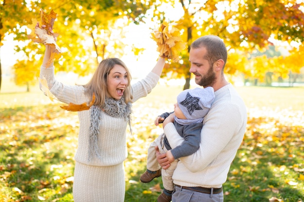 Beautiful family having fun with their child in autumn park.