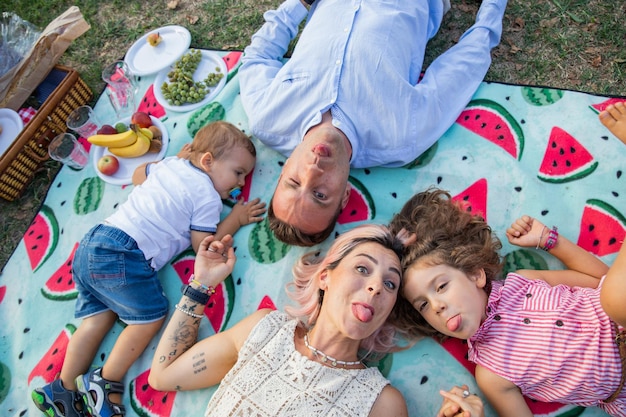 Beautiful family with small children at the park lying on the ground having picnic doing funny faces