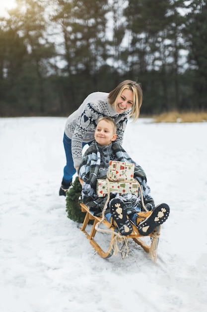 Beautiful family of young mother and son enjoying snowy winter day outdoors having fun sledging