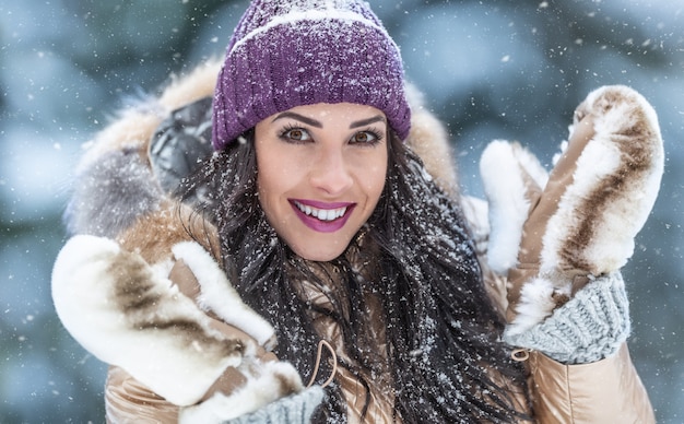 Beautiful fashion loving woman wears fur coat and furry gloves outdoors on a snowy day.