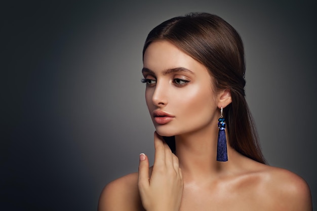 Beautiful Fashion Model Woman with Perfect Makeup and Blue Silky Jewelry Earrings on Background with Copy space