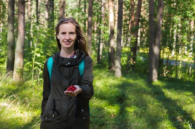 Bella donna moderna di moda che raccoglie un palmo pieno di fragole nella foresta.