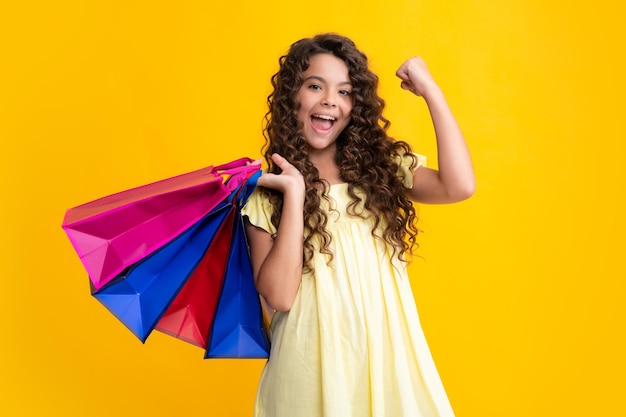 Beautiful fashion teenager child girl with shopping bags on yellow background shopaholic shopping and fashion kid with shopping sale bags excited teenager glad amazed and overjoyed emotions