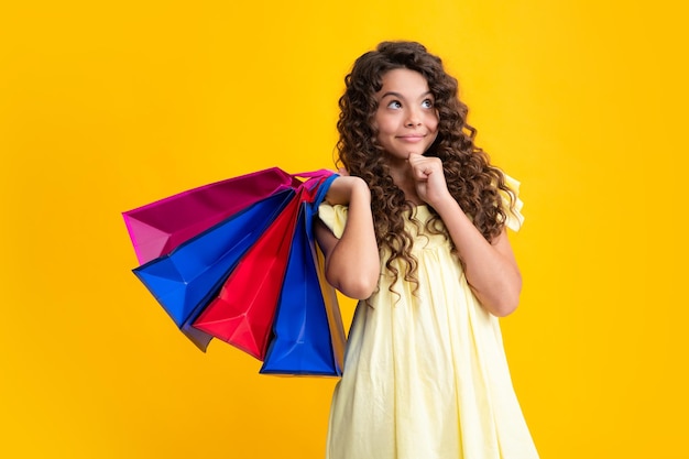 Beautiful fashion teenager child girl with shopping bags on yellow background Shopaholic shopping and fashion Kid with shopping sale bags Thinking face thoughtful emotions of teenager girl