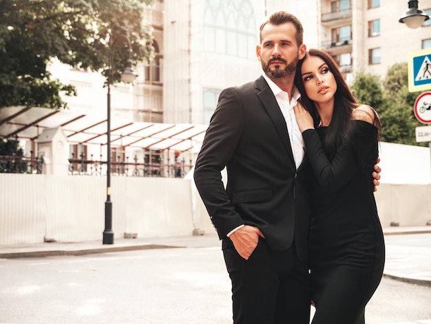 Beautiful fashion woman and her handsome elegant boyfriend in
suit sexy brunette model in black evening dress fashionable couple
posing in the street in europe brutal man and his female
outdoors