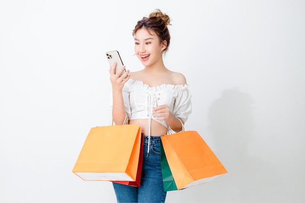 Beautiful fashionable asian woman holding shopping bags and using mobile phone on isolated white background and copy space Shopping online payment smile good mood