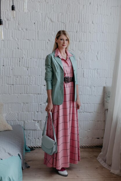 Beautiful fashionable blonde girl stands in a pink dress and a mint jacket with a bag in her hands