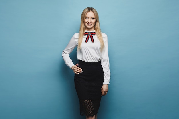 Photo beautiful and fashionable blonde model girl   in stylish blouse and black lace skirt, smiling and posing at studio at blue background