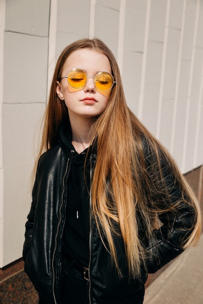 Beautiful fashionable kid girl with long hair in yellow sunglasses in city,