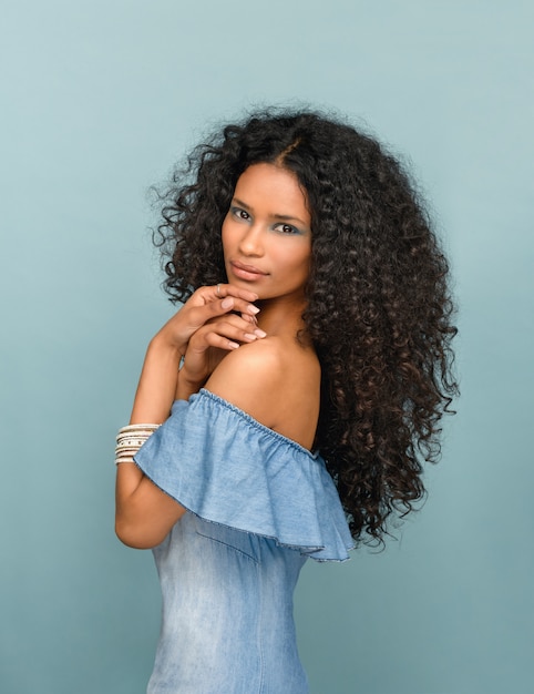 Bella giovane donna snella alla moda da santo domingo con lunghi capelli neri ricci sul blu