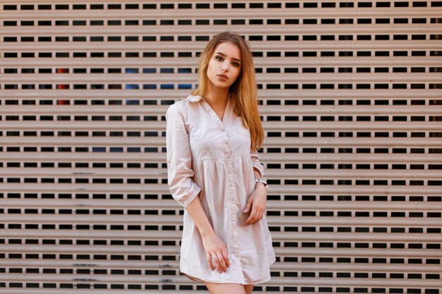 Beautiful fashionable woman in stylish clothes posing near a metal wall.