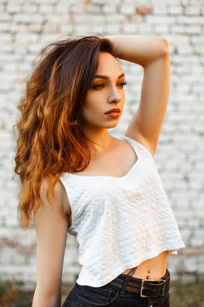 Beautiful fashionable woman with a haircut in a white tank top near a brick wall