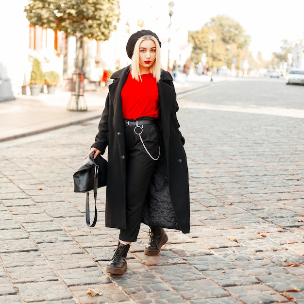 街を歩いて秋の日に黒いファッションコートのハンドバッグで美しいファッショナブルな女性