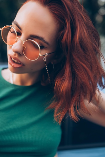 Beautiful fashionable young woman in glasses posing near car