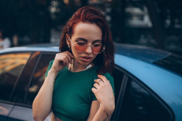 Beautiful fashionable young woman in glasses posing near car