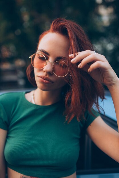 Beautiful fashionable young woman in glasses posing near car