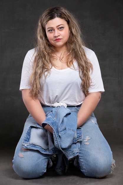 Beautiful fat woman in denim clothes on a gray background. Plus size model girl.