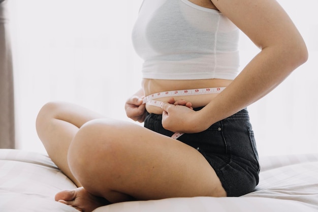 Beautiful fat woman with tape measure she uses her hand to\
squeeze the excess fat that is isolated on a white background she\
wants to lose weight the concept of surgery and break down fat\
under the