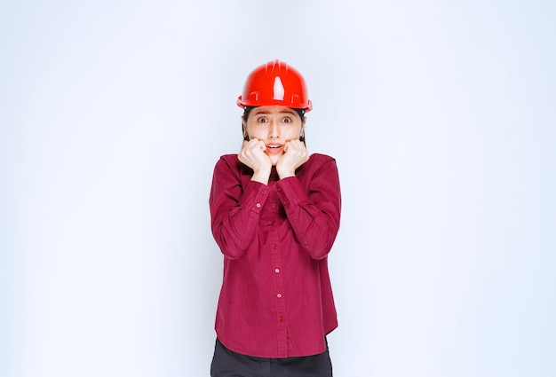 Beautiful female architect in red hard helmet scared of something. 