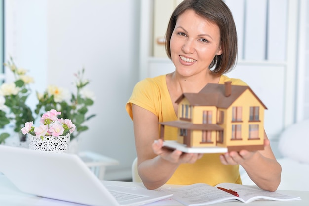 Beautiful female architect working in modern office holding house model