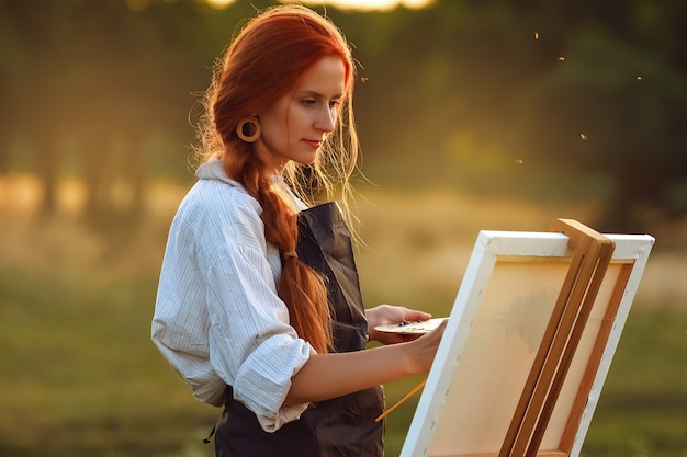 Beautiful female artist painting at sunset in nature