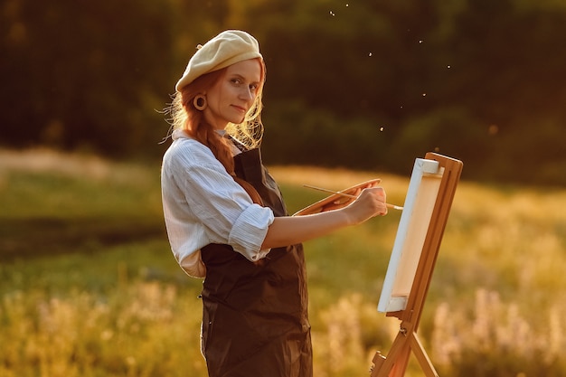 Beautiful female artist painting at sunset in nature