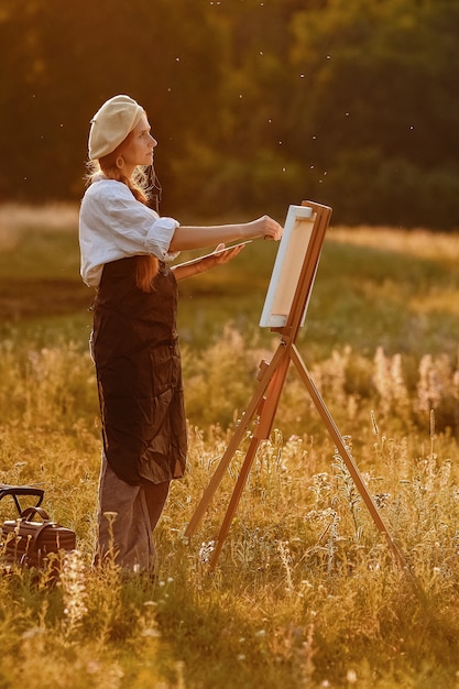 Beautiful female artist painting at sunset in nature