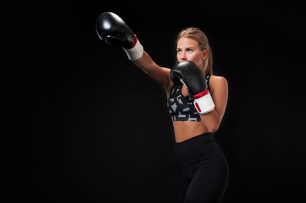 Beautiful female athlete in boxing gloves, in the studio on a black background. The boxer fulfills the blow